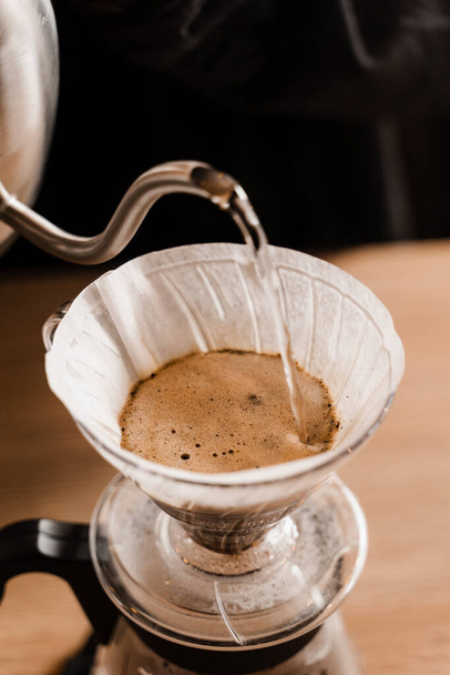 Close-up pour over filter with ground coffee in the funnel in focus. Drip filter coffee brewing. Pour over alternative method of pouring water over roasted and ground coffee beans contained in filter - Photo, Image