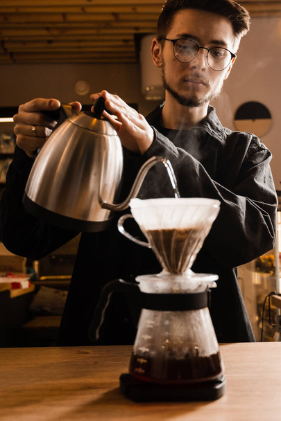 Kaada suodatin kahvi vaihtoehtoinen panimomenetelmä. Barista kaataa kuumaa vettä paahdettujen ja jauhettujen kahvipapujen päälle, jotka sisältyvät paperisuodattimeen - Valokuva, kuva