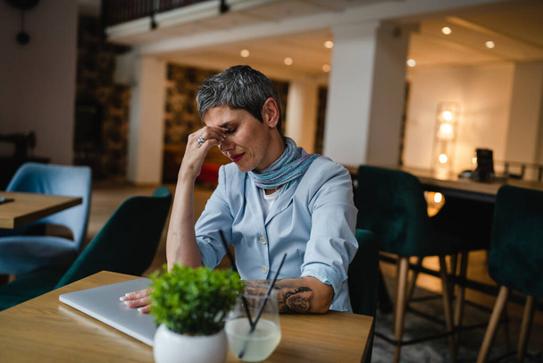 One woman entrepreneur or business senior female sit at the table at cafe with laptop overworked have headache hold head worried about problems at work bad emotion copy space - Fotoğraf, Görsel