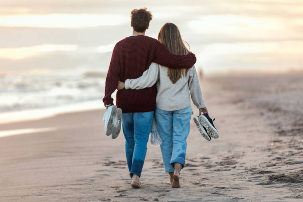 Portrait of beautiful young couple in love walking together in a cold winter day on the beach. - 写真・画像