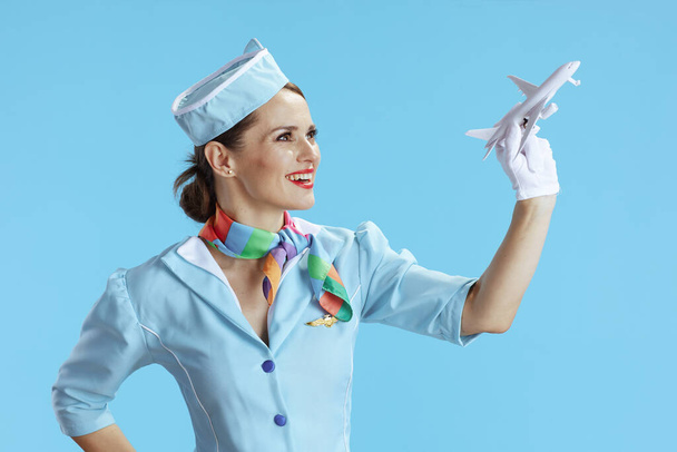 smiling modern female air hostess isolated on blue background in blue uniform with a little airplane. - 写真・画像