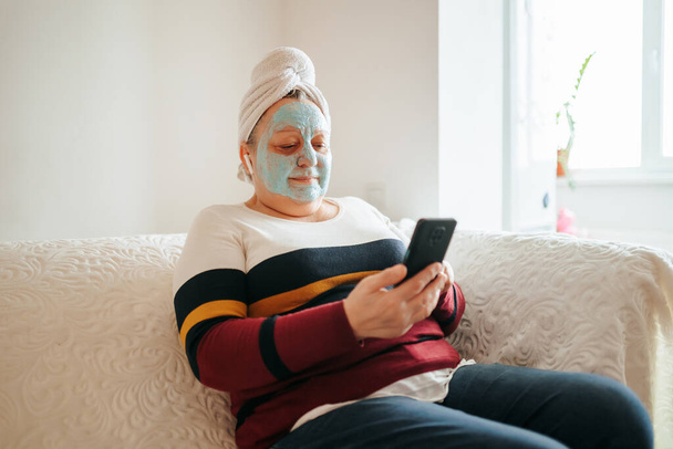 Real People and Real Skincare A photo of a pretty, old woman enjoying her skincare routine in her living room with a mask on her face and music playing in the background. authenticity and reality - Valokuva, kuva