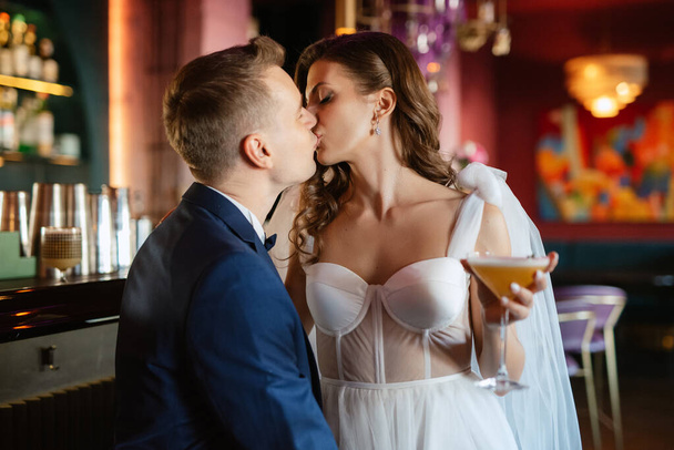 bride and groom inside a cocktail bar in a bright atmosphere with a glass of drink - Fotografie, Obrázek