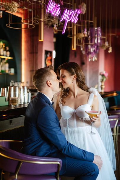 bride and groom inside a cocktail bar in a bright atmosphere with a glass of drink - Photo, image