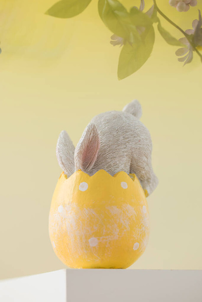 Easter card with a rabbit in an egg on a podium on a yellow background with flowers. The concept of a happy Easter. - Фото, зображення