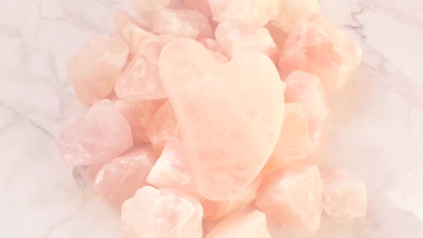 gua sha scraper.Rose quartz massage grattoir en forme de coeur de pierre naturelle sur quartz rose sur fond de marbre gris. appareil de massage du visage. Images 4k - Séquence, vidéo