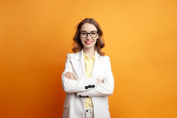 young business woman in glasses and white suit stands with her arms crossed on colored isolated background, manager girl in office style on yellow background - Valokuva, kuva