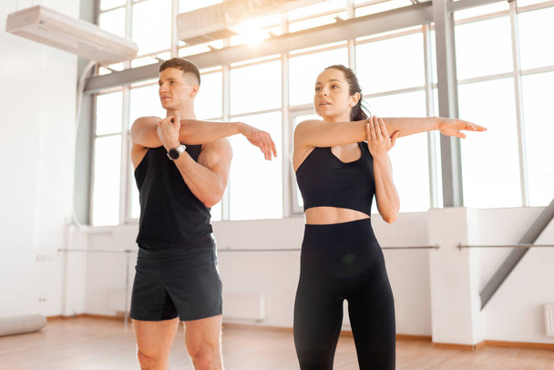 beautiful athletic couple in sportswear warm up in the gym in the morning, fitness girl and coach man go in for sports in training in bright room - Foto, imagen
