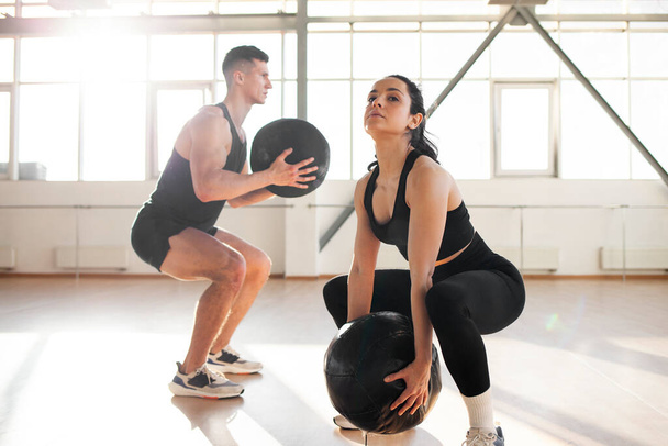 young beautiful athletic couple in sportswear at crossfit training with ball in the fitness room, woman and man together at fitness training go in for sports and do endurance exercise - Photo, Image