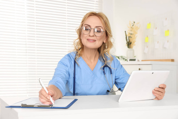 Doctor with glasses and tablet consulting patient in clinic. Online medicine concept - Photo, Image