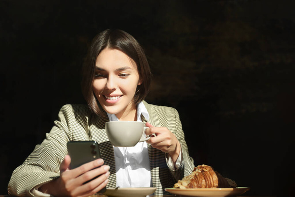 Special Promotion. Happy young woman with cup of drink using smartphone at table in cafe - Фото, изображение