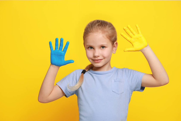 Little girl with hands painted in Ukrainian flag colors on yellow background. Love Ukraine concept - Fotoğraf, Görsel