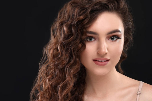 Beautiful young woman with long curly brown hair on black background, closeup. Space for text - Foto, afbeelding