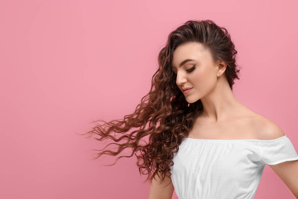 Beautiful young woman with long curly brown hair on pink background, space for text - Valokuva, kuva