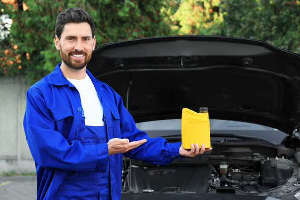 Smiling worker showing yellow container of motor oil near car outdoors - Fotografie, Obrázek