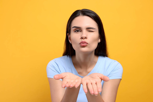 Beautiful young woman blowing kiss on yellow background - Photo, image