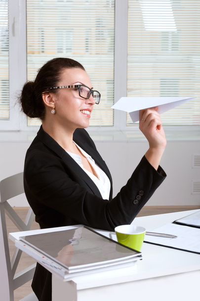 Woman in a suit sitting at table in office throwing paper airpla - 写真・画像