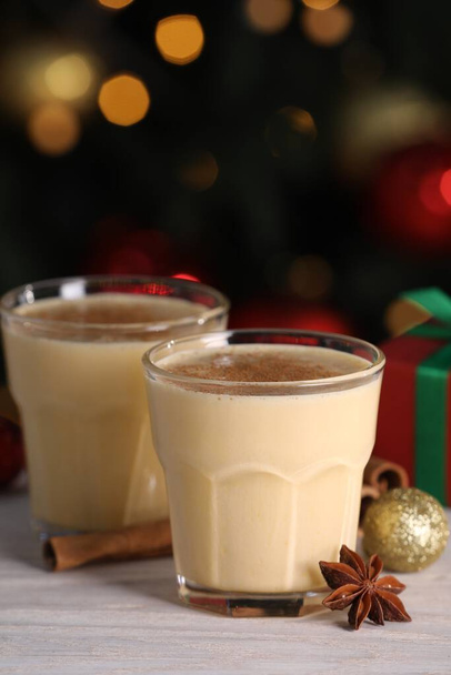 Tasty eggnog, cinnamon, anise and Christmas decorations on white wooden table against blurred lights - Φωτογραφία, εικόνα