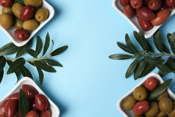Different fresh olives and green leaves on light blue background, flat lay. Space for text - Φωτογραφία, εικόνα