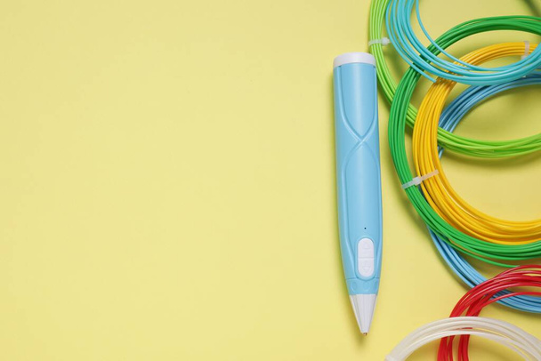 Stijlvolle 3D-pen en kleurrijke plastic filamenten op lichtgele achtergrond, vlakke lay. Ruimte voor tekst - Foto, afbeelding