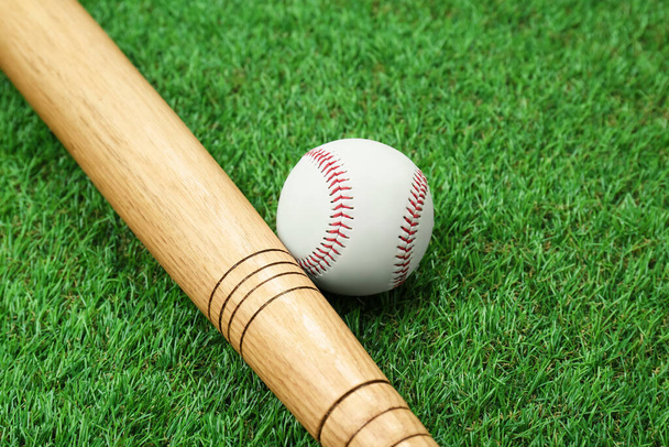 Wooden baseball bat and ball on green grass, closeup. Sports equipment - Fotografie, Obrázek