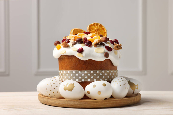 Традиционный пасхальный торт с сухофруктами и украшенными яйцами на белом деревянном столе в помещении - Фото, изображение