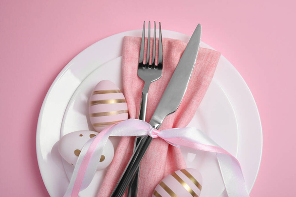 Festive table setting with painted eggs and cutlery on pink background, above view. Easter celebration - Φωτογραφία, εικόνα
