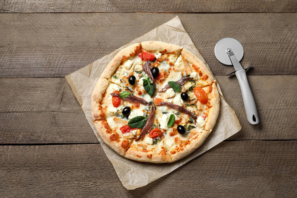 Tasty pizza with anchovies and cutter on wooden table, top view - Foto, Imagem