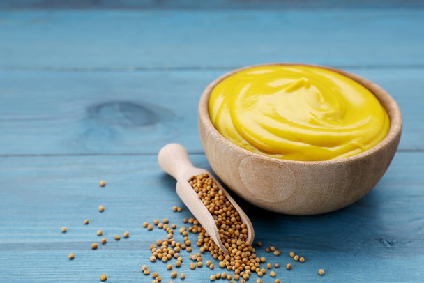 Sauce bowl with delicious mustard and seeds on light blue wooden table, closeup. Space for text - Fotografie, Obrázek