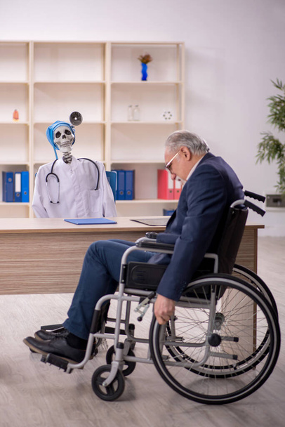 Tekerlekli sandalyedeki yaşlı hasta şeytan doktoru ziyaret ediyor. - Fotoğraf, Görsel
