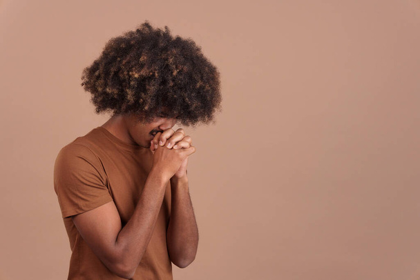 Homem africano com cabelo encaracolado rezando com as mãos dobradas e olhos fechados em estúdio - Foto, Imagem