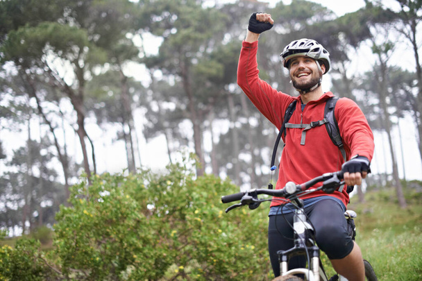 This feels great. A young male athlete pumping his fist in the air after conquering a mountain biking trail - Фото, зображення
