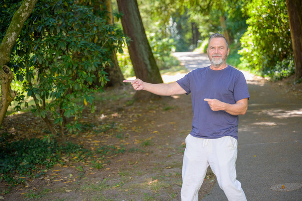 Man van middelbare leeftijd die over een landweg loopt met schaduwrijke bomen die naar de zijkant naar copyspace wijzen - Foto, afbeelding