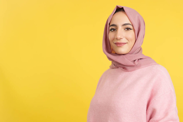 Szczęśliwa muzułmanka w hidżabie patrząca w kamerę w studio z żółtym tłem - Zdjęcie, obraz