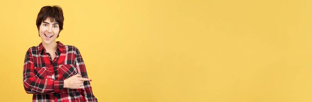 Persona andrógina apuntando a un espacio en blanco en estudio con fondo amarillo - Foto, Imagen
