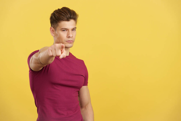 Handsome caucasian man pointing to camera with index finger in studio with yellow background - Foto, Imagen