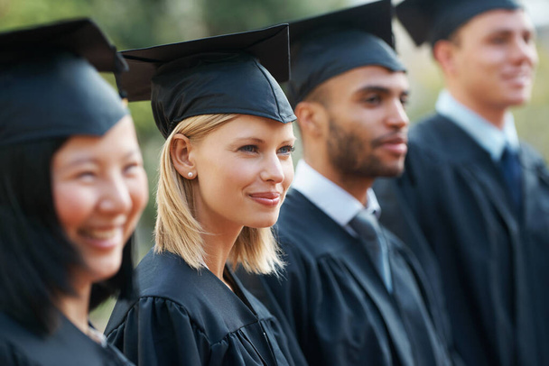 De cara a su futuro. Jóvenes graduados universitarios sosteniendo sus diplomas mientras están de pie en una fila y sonriendo - Foto, Imagen