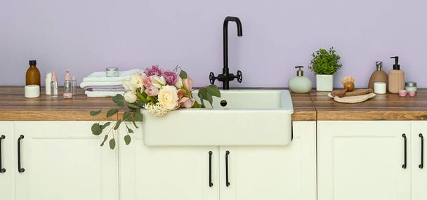 Víznyelő gyönyörű friss virágokkal és fürdőfelszereléssel az orgonafal mellett - Fotó, kép