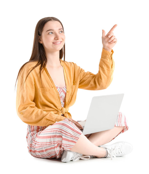 Jolie jeune femme avec ordinateur portable pointant quelque chose tout en étant assis sur fond blanc - Photo, image