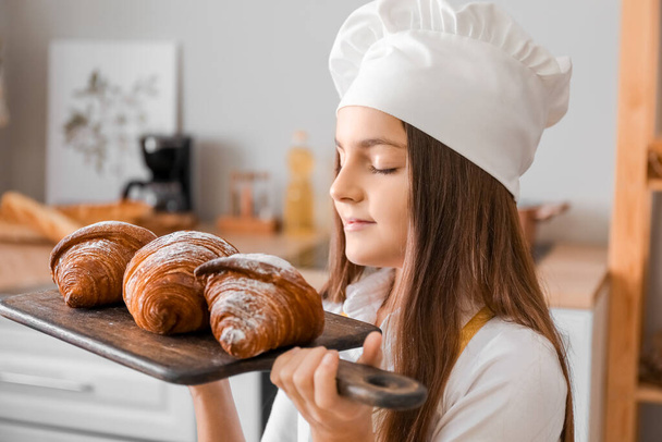 Little baker with board of tasty croissants in kitchen, closeup - Foto, imagen