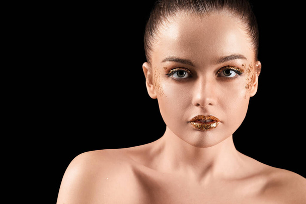 Young woman with golden glitter makeup on black background, closeup - Valokuva, kuva