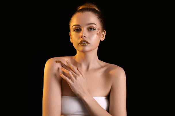 Young woman with golden glitter makeup on black background - Photo, image