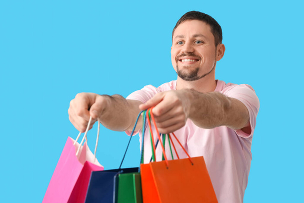 Hombre guapo con bolsas de compras sobre fondo azul - Foto, imagen