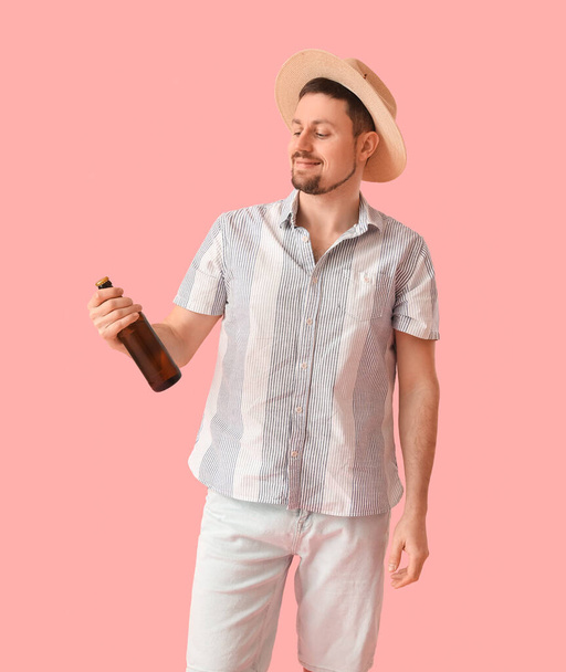 Handsome man in straw hat with bottle of beer on pink background - Foto, imagen