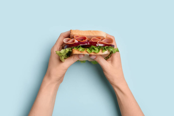 Female hands holding delicious ham sandwich on blue background - Foto, afbeelding