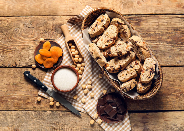 Cesta con deliciosas galletas de biscotti, chocolate, albaricoques secos y avellanas sobre fondo de madera - Foto, imagen