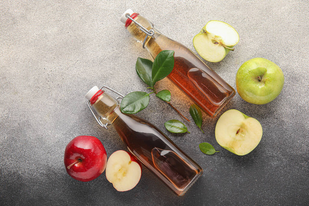 Bouteille en verre de vinaigre de cidre de pomme frais et fruits sur fond gris grunge - Photo, image