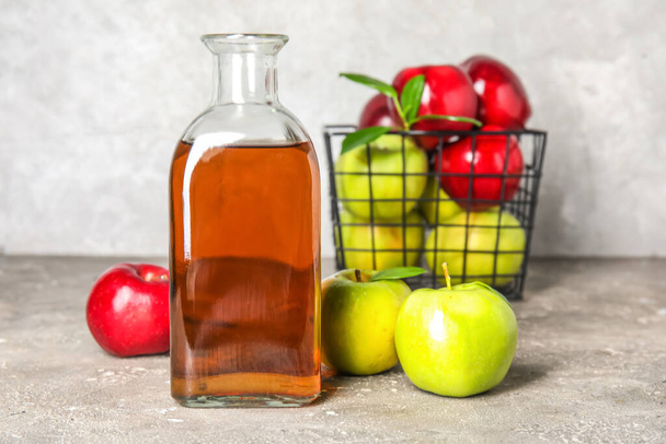 Lasipullo tuoretta omenaviinietikkaa ja hedelmiä harmaalla grunge-pöydällä - Valokuva, kuva