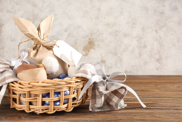 Basket with Easter eggs and bunny gift bag on wooden table against grunge wall - Fotoğraf, Görsel