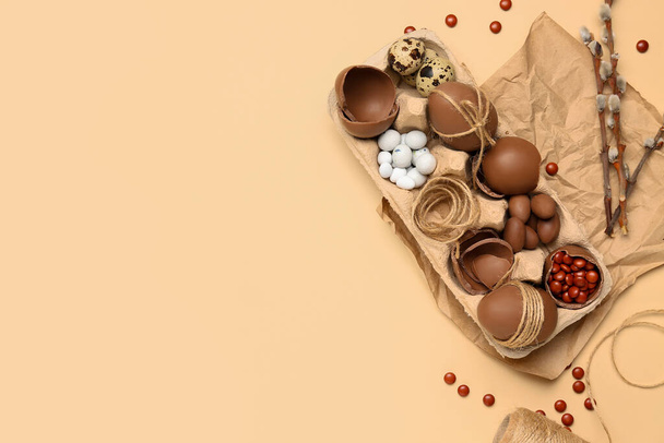 Houder met chocolade paaseieren, snoepjes en wilgentakken op beige achtergrond - Foto, afbeelding